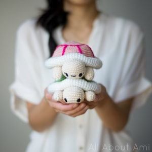 Op de afbeelding: Twee gehaakte amigurumi schildpad speelgoed op elkaar gestapeld. De bovenste schildpad heeft een roze schild en de onderste schildpad heeft een groene schild. Beide schildpadden hebben een wit lichaam en zwarte ogen.