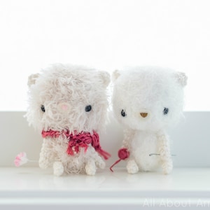 May include: Two white crocheted stuffed animals with black eyes. One is wearing a red scarf.