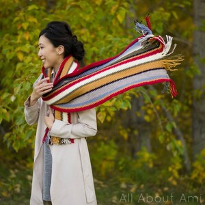May include: A woman wearing a beige coat with a colorful striped crocheted scarf with fringe. The scarf is blowing in the wind.