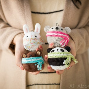 May include: Four crocheted animal ornaments with scarves. A white bunny, a brown bear, a gray koala, and a black and white panda.
