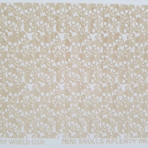 May include: A white sheet of paper with a pattern of beige mini skulls. The text "ART CLAY WORLD USA" and "MINI SKULLS APLENTY INVERSE" is printed at the bottom of the sheet.