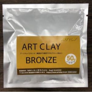 May include: A silver-colored, sealed foil pouch containing 50g of Art Clay Bronze. The label is yellow with black text reading ART CLAY BRONZE, Japanese characters, and a white circle with 50g printed inside. The bottom includes manufacturer details.