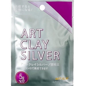 May include: A silver-colored rectangular foil packet labeled ART CLAY SILVER in large dark text. The packaging features a purple triangular accent at the top, a circular 5g weight indicator at the bottom left, and Japanese text throughout the front.