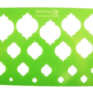 May include: Green plastic stencil with 12 cut-out shapes. The shapes are a traditional Moroccan design. The stencil is labeled "ArtClayWorld USA Arabesque Shapes".