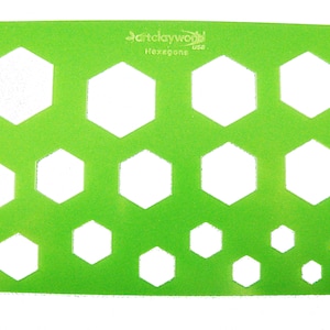 May include: Green plastic stencil with multiple hexagon shapes of varying sizes. The stencil is labeled "Hexagons" and "Clayworld use".