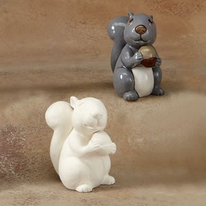 May include: Two ceramic squirrel figurines, one gray and one white, each holding a nut in their paws.