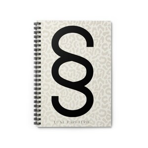May include: A spiral bound notebook with a beige leopard print background and a large black section symbol. The text "LUXE PAPETERIE" is printed at the bottom of the notebook.
