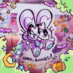 May include: A sticker featuring a cartoon bunny with purple fur, white eyes, and a black X over each eye. The bunny is wearing a white heart on its chest and has a pink nose. The sticker has the text "OMG, BOOBS!" printed on it.