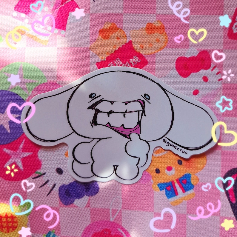 May include: A white cartoon sticker with a grinning character, featuring black outlines and pink accents on the mouth. The sticker is on a pink patterned background with hearts and stars. The artist's signature, @gumicroc, is visible.
