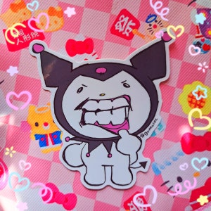 May include: A white sticker featuring a cartoon character with a black hood, a large grin, and a devil tail. The character is on a pink and white checkered background with hearts and other cartoon characters.