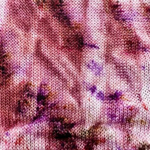 Può includere: Primo piano di un tessuto a maglia con un motivo tie-dye in tonalità rosa, viola e marrone.