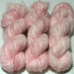 Pode incluir: Três novelos de fio macio e rosa com uma textura felpuda.