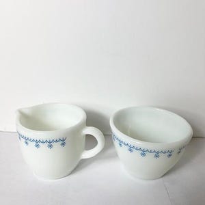 May include: A white creamer and sugar bowl set with a blue snowflake pattern.