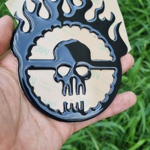 May include: Black skull with flames decal. The skull is surrounded by a circle of flames. The decal is on a white background.