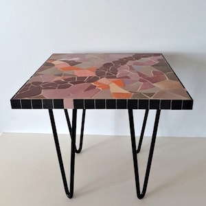 Peut inclure: Une table d'appoint carrée avec un plateau en mosaïque de carreaux dans des tons de rose, violet et orange. La table a des pieds en épingle à cheveux noirs.