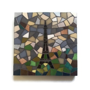 May include: A mosaic artwork depicting the Eiffel Tower in black against a background of colorful, broken glass tiles. The tiles are arranged in a random pattern, creating a textured and abstract effect. The colors include shades of blue, green, brown, and beige.