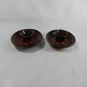 May include: Two ceramic dishes with a dark brown centre and a reddish-brown outer ring. Each dish has a small, matching bowl in the centre. The dishes are likely for serving dips or sauces.