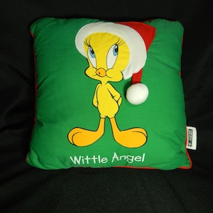 May include: A green square pillow featuring Tweety Bird wearing a Santa hat. The cartoon character is yellow with orange feet and a beak. The pillow has a red border and the words "Wittle Angel" are printed on the front.