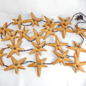 May include: A string of decorative lights featuring multiple starfish-shaped ornaments. The starfish are a light brown color and are connected by a dark brown wire. The string has a brown plug.