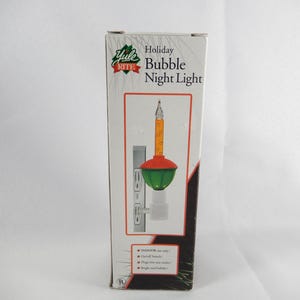 May include: A Yule Rite Holiday Bubble Night Light product box. The packaging features a graphic of a plug-in night light with a green base, a red top, and an orange bubble tube. The box includes text reading Yule Rite Holiday Bubble Night Light.