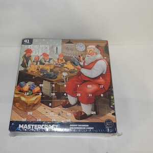 May include: A Mastercraft Advent Calendar featuring Santa Claus in a red suit working in a workshop with elves. The calendar has 24 numbered doors, each with a small window to reveal a surprise behind it. The calendar is decorated with a festive Christmas tree and other holiday elements.