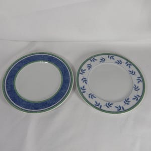 May include: Two white ceramic plates with blue and green decorative borders. One plate has a blue and green patterned border, the other a leaf design in blue and green. Suitable for serving food, these plates are approximately 20 cm in diameter.