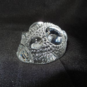 Può includere: Oggetto decorativo in vetro trasparente con superficie strutturata e forma arrotondata. L'oggetto presenta molteplici protuberanze a forma di bolla e una qualità riflettente, suggerendo che sia fatto di cristallo o materiale simile.