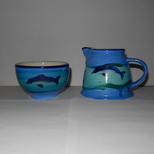 Könnte beinhalten: Ein blaues und grünes Keramik-Set aus Milchkännchen und Zuckerdose mit Delfin-Motiv.