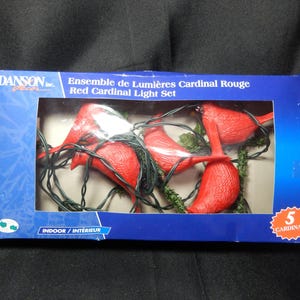 May include: A blue box shows a Red Cardinal Light Set. The set features five red cardinal bird ornaments with green leaves and black wiring. The box reads "Indoor/Interieur".