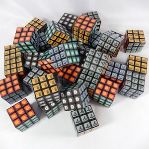 May include: A pile of Halloween-themed Rubik's Cubes. The cubes display orange, green, and black designs with Halloween icons. The cubes are scattered on a white surface, highlighting their colourful and intricate patterns.