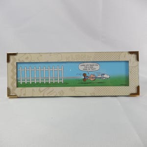 Puede incluir: Un marco rectangular con una impresión de una escena de dibujos animados con una valla blanca, hierba verde y un cielo azul. La impresión incluye el texto: "When life takes you for a ride, hang on tight!" El marco tiene esquinas decorativas.