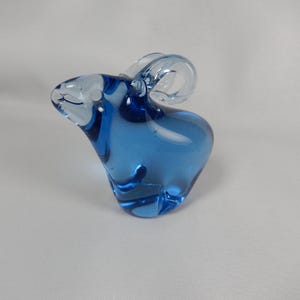 May include: A blue glass mouse ornament with large, clear ears. The mouse has a rounded body and a lighter, almost white, glass face. This decorative figurine is likely for display, a charming home accent.