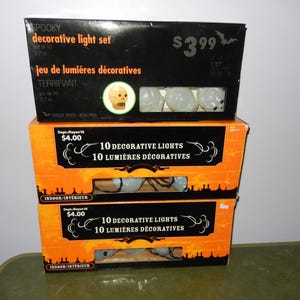 May include: Three packs of Halloween lights featuring a spooky skull design. The top pack is black with white text and a price tag of £3.99. The bottom two packs are orange and black with a price tag of £4.00. The text on the packs reads "10 Decorative Lights" and "10 Lumières Décoratives".
