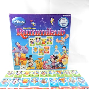 以下が含まれることがあります： ディズニーキッズ版ラミィキューブのゲームボックス。紫色の箱にはディズニーのロゴとゲームタイトルが表示されています。ゲームには、ミッキーマウスやプーさんなどのキャラクターが描かれたタイルが含まれています。