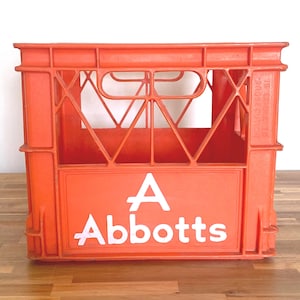 May include: A bright orange plastic storage crate featuring a grid-like structural design with integrated handles. The front panel displays the white text A Abbotts in a bold, sans-serif font, while the side panel includes embossed text.