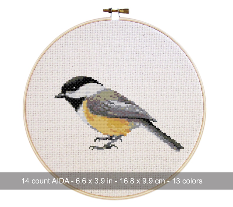 May include: A cross-stitch embroidery of a chickadee bird, featuring black, white, gray, and yellow hues. The bird is centered on a white AIDA cloth, framed by a wooden hoop. The text at the bottom reads: 14 count AIDA - 6.6 x 3.9 in - 16.8 x 9.9 cm - 13 colors.