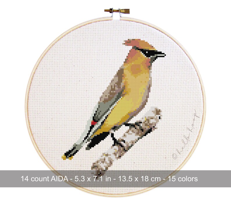 May include: A cross-stitch embroidery of a bird with yellow, brown, and black plumage perched on a branch. The artwork is framed in a wooden hoop. The text on the image reads: 14 count AIDA - 5.3 x 7.1 in - 13.5 x 18 cm - 15 colors.