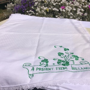 May include: White linen tea towel with green embroidered shamrocks and the text "A present from Ireland".