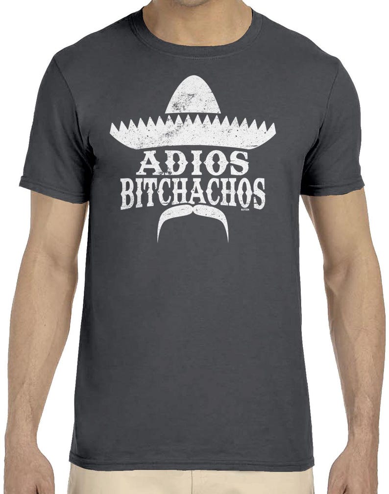 Op de afbeelding: Donkergrijs t-shirt met een witte sombrero-afbeelding, snor en de tekst "ADIOS BITCHACHOS". De afbeelding heeft een vintage uitstraling. Het t-shirt heeft korte mouwen en is gemaakt van zacht materiaal.