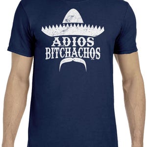 Op de afbeelding: Marineblauw t-shirt met een witte sombrero-afbeelding, de woorden "ADIOS BITCHACHOS" en een witte snor. De afbeelding heeft een vintage uitstraling. Het shirt heeft een ronde hals.