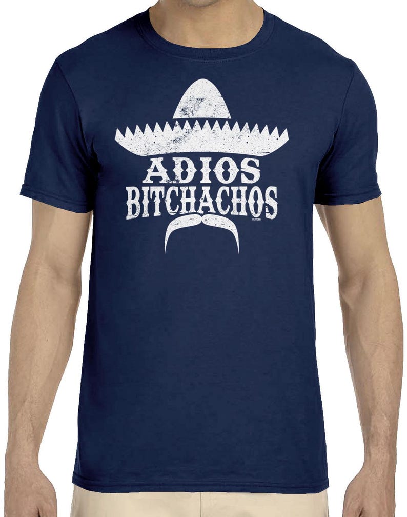 Op de afbeelding: Marineblauw t-shirt met een witte sombrero-afbeelding, de woorden "ADIOS BITCHACHOS" en een witte snor. De afbeelding heeft een vintage uitstraling. Het shirt heeft een ronde hals.
