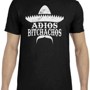 Op de afbeelding: Zwart t-shirt met een witte sombrero-afbeelding, een gestileerde snor en de tekst "ADIOS BITCHACHOS". Het ontwerp is op de voorkant gedrukt. Het t-shirt is gemaakt van een zacht, comfortabel materiaal.
