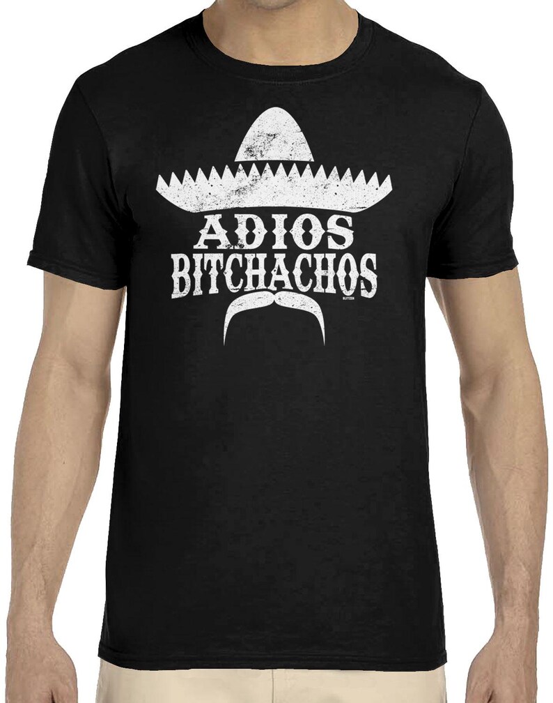 Op de afbeelding: Zwart t-shirt met een witte sombrero-afbeelding, een gestileerde snor en de tekst "ADIOS BITCHACHOS". Het ontwerp is op de voorkant gedrukt. Het t-shirt is gemaakt van een zacht, comfortabel materiaal.