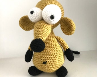 Puede incluir: Un animal de peluche de crochet con forma de ratón con grandes ojos blancos y pupilas negras. El ratón es marrón y tiene patas negras y una nariz negra. El ratón está sentado en un estante blanco.