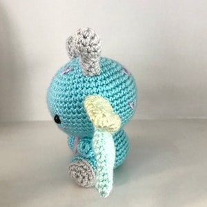May include: A light blue crocheted stuffed animal with gray and yellow accents. The animal has two horns and a tail.