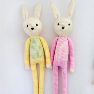 May include: Two crocheted bunny toys, one yellow with a light blue and yellow striped shirt and one pink with a pink and white striped shirt.