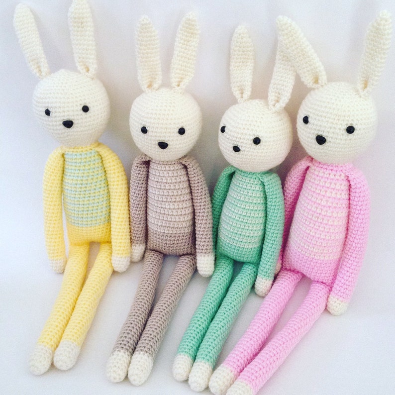 May include: Four crocheted bunny rabbit toys in different colors. The bunnies are yellow, gray, green, and pink. Each bunny has black eyes and a white nose.
