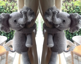 May include: Two gray crocheted elephant curtain tiebacks holding back a pair of cream curtains.