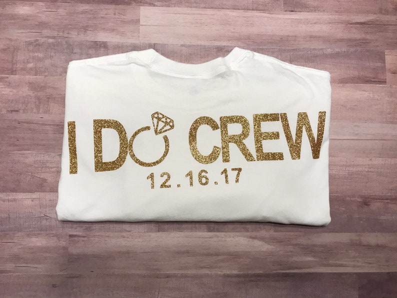 May include: White t-shirt with gold glitter lettering that says "I DO CREW" with a diamond ring graphic and the date "12.16.17".