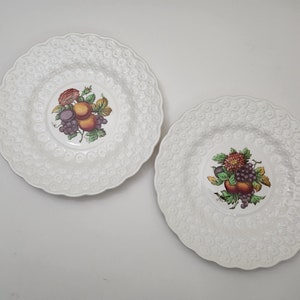 May include: Two white ceramic plates with raised floral designs. Each plate features a colorful fruit and flower design in the center.